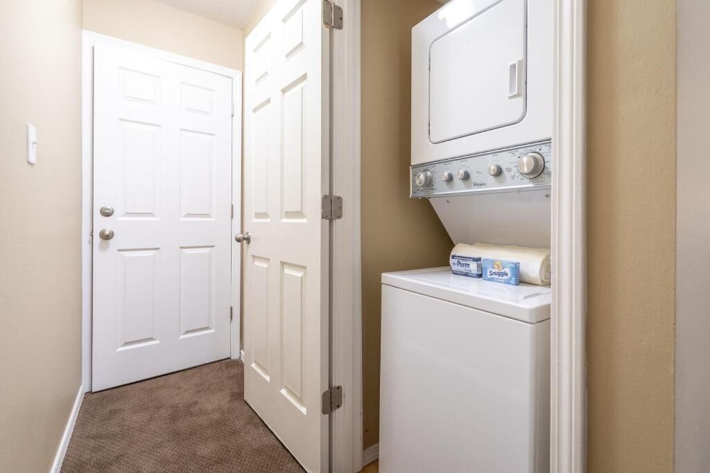 A laundry room with a front-loading washer and dryer, a door, and a carpeted floor.