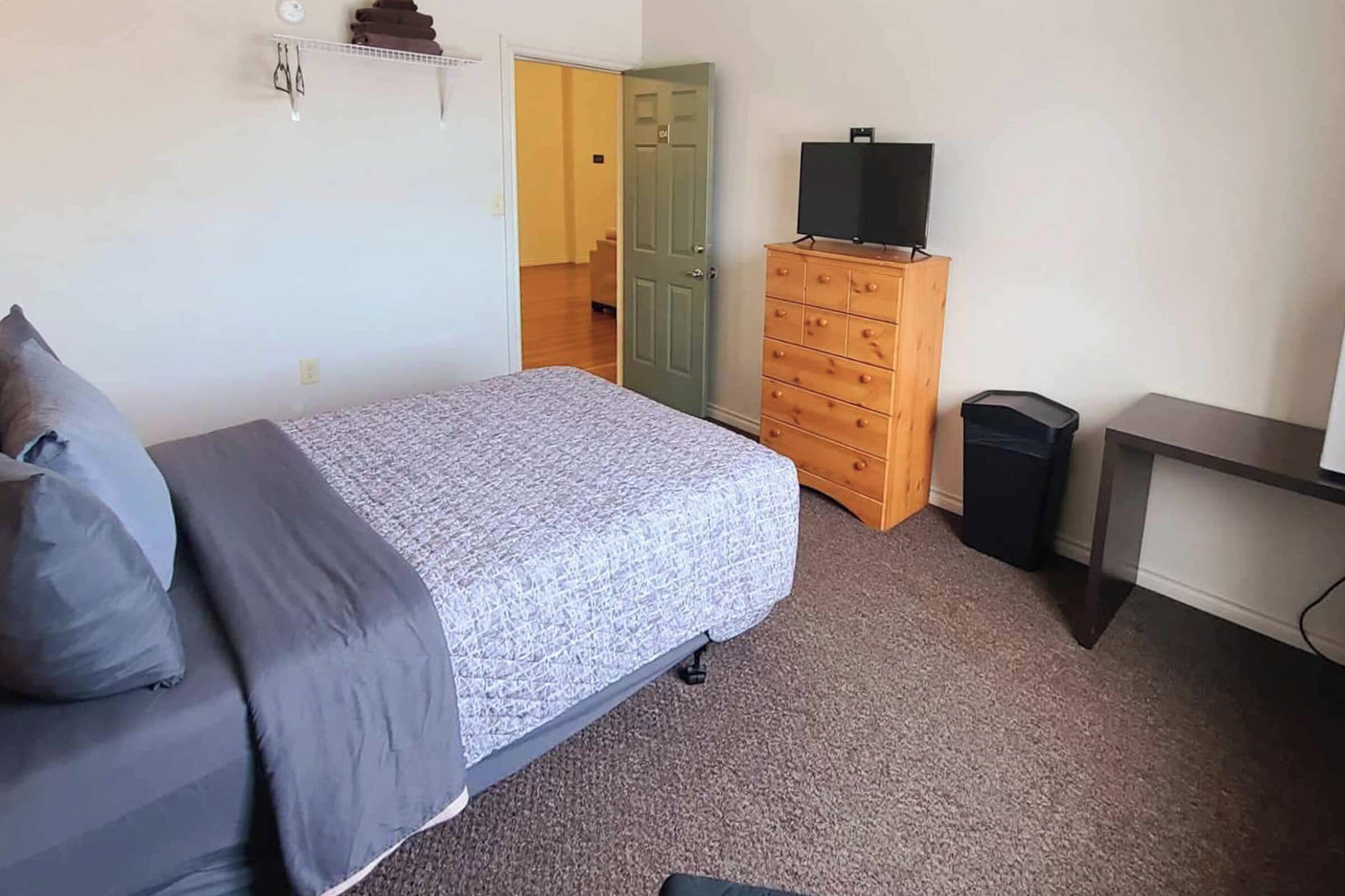 Quarto com cama, penteadeira, televisão e lixeira.