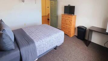 Quarto com cama, penteadeira, televisão e lixeira.