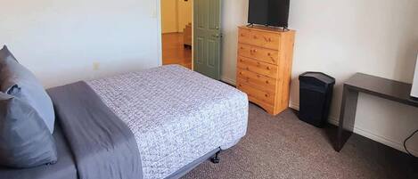 A bedroom with a bed, a dresser, a television, and a trash bin.
