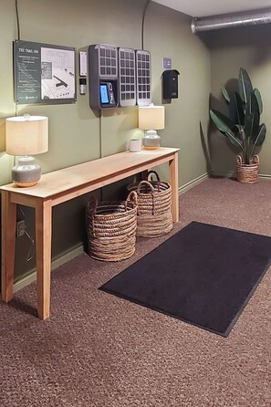 A reception area with a wooden bench, two woven baskets, a black mat, a wall-mounted information board, and a potted plant. - WorkStay Lodging - Yarbo, SK - Near Esterhazy & Mosaic K1, K2, & K3 (Yarbo)