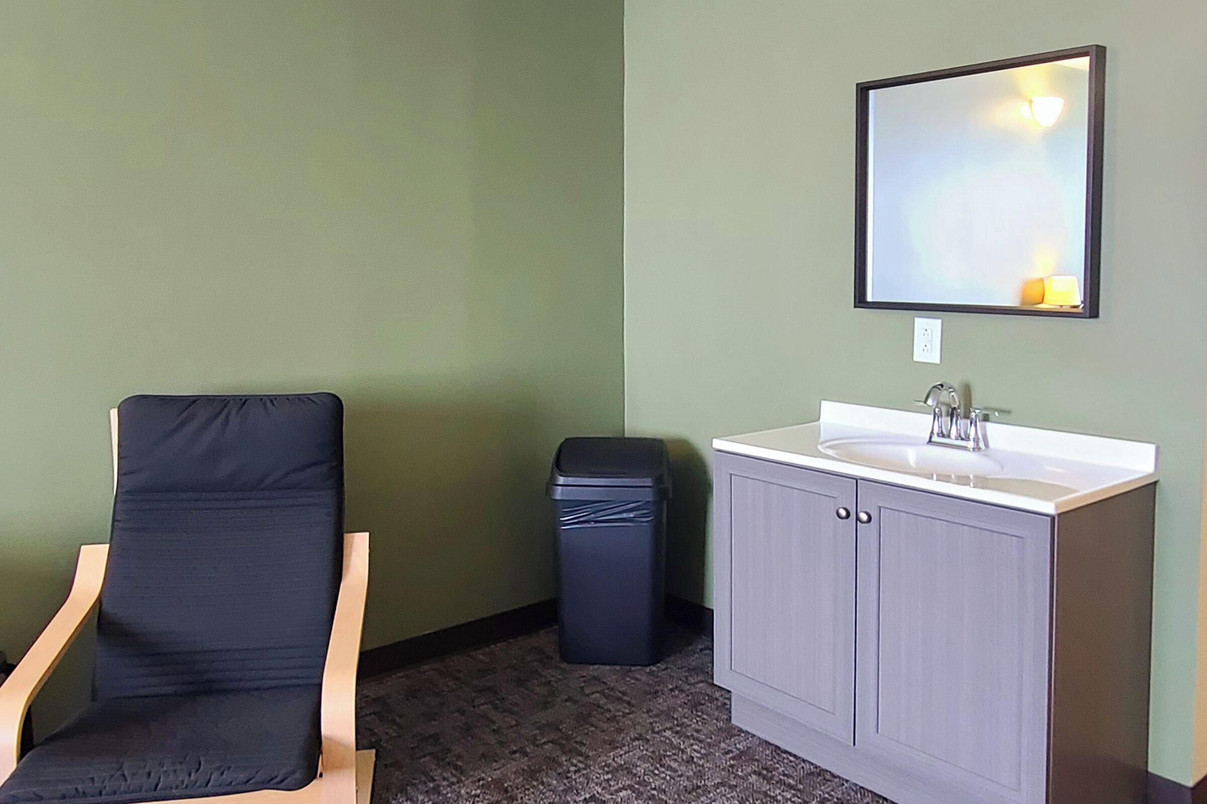 A room with a single chair, a sink, and a trash bin.