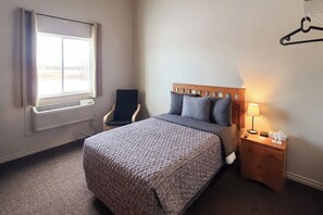 A hotel room with a bed, a chair, a bedside table with a lamp, and a window with curtains. - WorkStay Lodging - Yarbo, SK - Near Esterhazy & Mosaic K1, K2, & K3 (Yarbo)