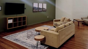 Een woonkamer met een bank, twee ronde tafels, een televisie en een kast.