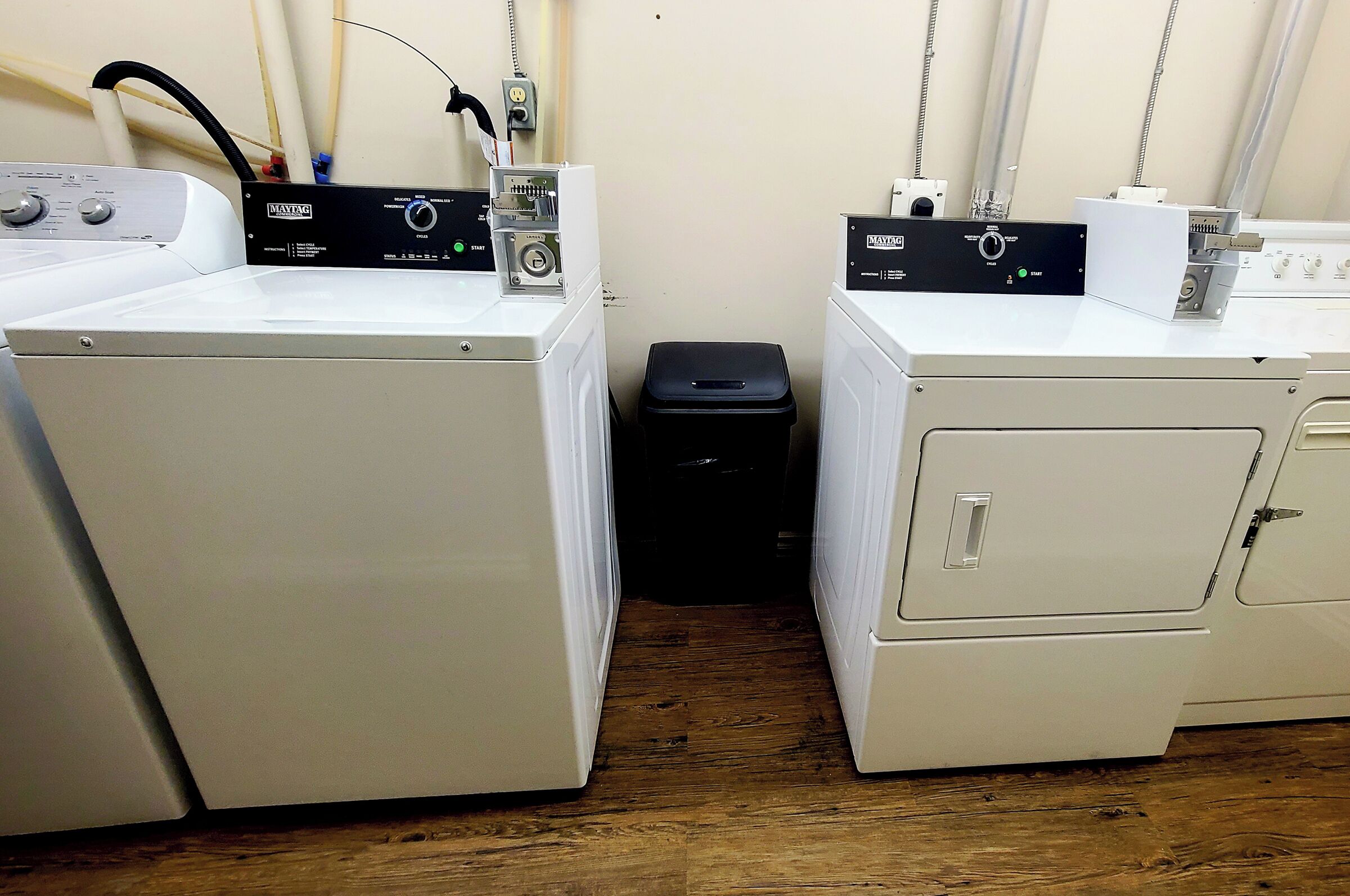 A laundry area with two front-loading washing machines and a small trash bin.