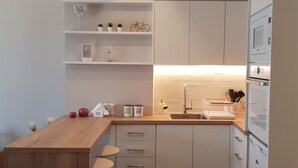 A modern kitchen with white cabinets, a wooden island with stools, a built-in oven, and a countertop with a sink. - ELEGANT HOUSE WITH ACROPOLIS VIEW (ΑΘΗΝΑ)