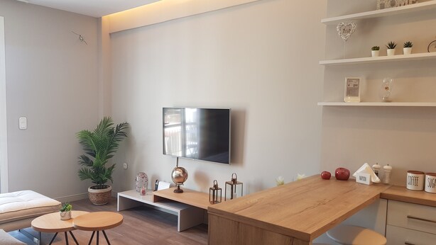 A modern living room with a wooden dining table, a flat-screen TV mounted on the wall, a potted plant, and a sofa. - ELEGANT HOUSE WITH ACROPOLIS VIEW (ΑΘΗΝΑ)