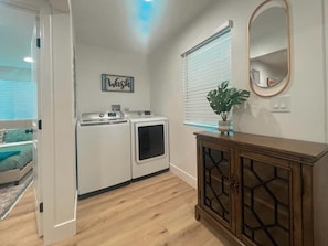 Compact laundry room with washer and dryer, storage cabinet, and potted plant.