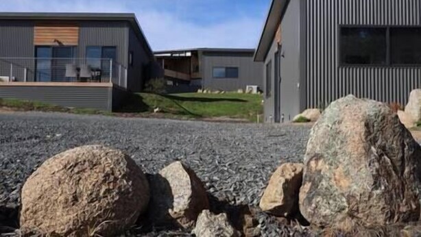 A modern building with a flat roof, large windows, and a gravel driveway.