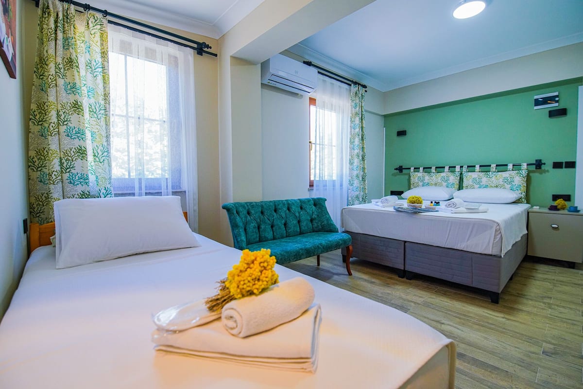 A hotel room with two beds, a green upholstered chair, and a bedside table with a flower arrangement.