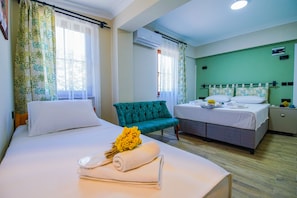 Una habitación de hotel con dos camas, una butaca tapizada de verde y una mesita de noche con un arreglo floral.