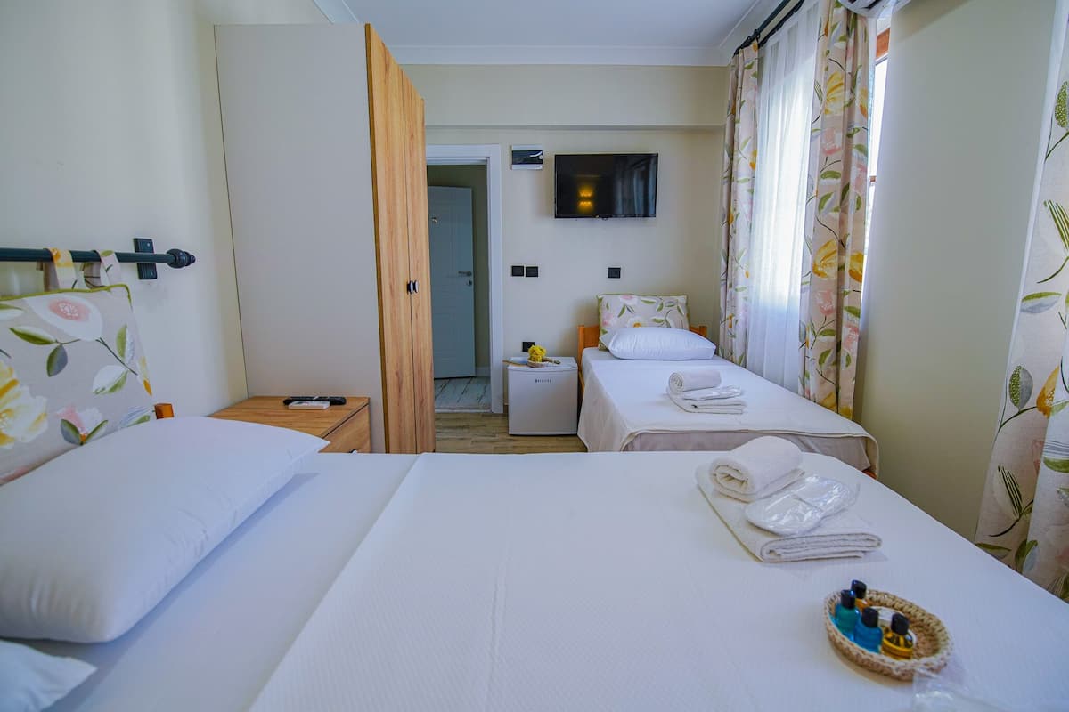 A hotel room with two beds, a TV on the wall, a small table with toiletries, and a door leading to another room.