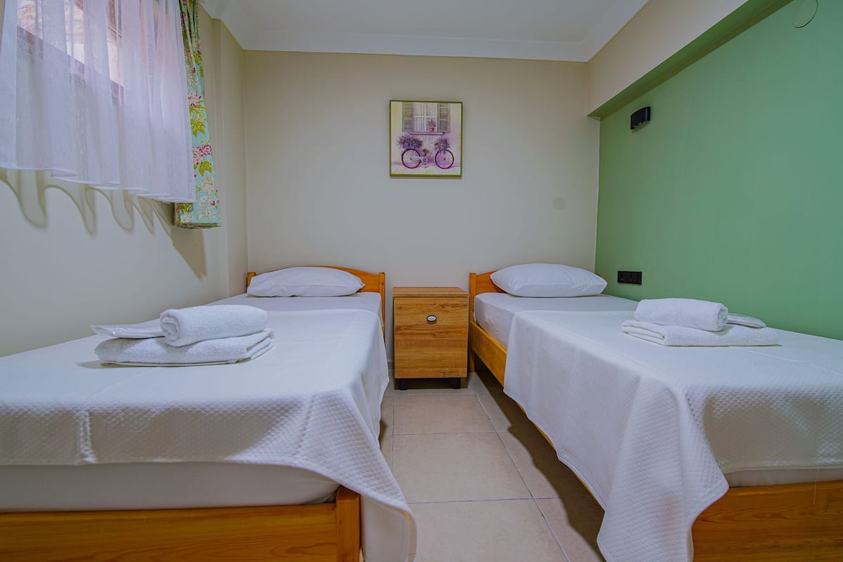 A room with two single beds, a wooden nightstand, a small table, and a wall-mounted picture.