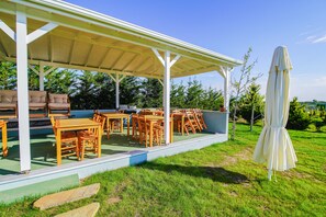 An outdoor patio with wooden tables and chairs, a covered seating area, and a white umbrella. - Keyf-i Ada Bozcaada (Bozcaada)