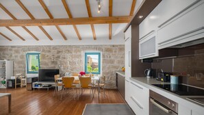 Una cocina moderna con vigas de madera, paredes de piedra y un comedor con televisor y sillas.