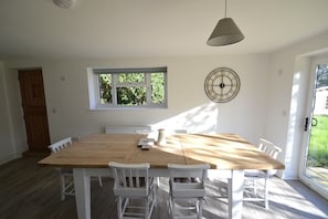 Un comedor con una mesa de madera y sillas blancas, una ventana y una puerta.
