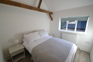 Un dormitorio con cama, mesitas de noche, ventana y radiador.