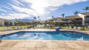 A swimming pool with lounge chairs and a covered area, surrounded by buildings and palm trees. - Hale Kamaole #166, VIEW, No Steps to Entry, Pool, A+ Wi-Fi, King Bed, EZ Parking (Kihei)