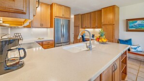 A modern kitchen with wooden cabinets, a stainless steel refrigerator, a granite countertop, and a sink. - Hale Kamaole #166, VIEW, No Steps to Entry, Pool, A+ Wi-Fi, King Bed, EZ Parking (Kihei)