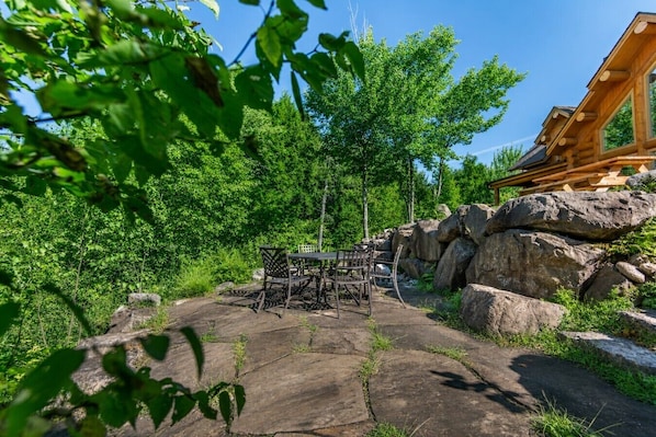 An outdoor seating area with a table and chairs, surrounded by large rocks and greenery.
