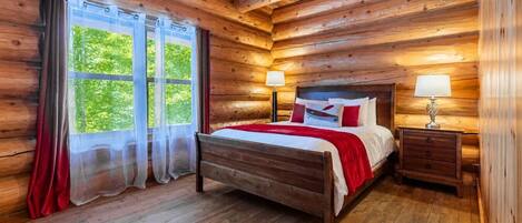 Une chambre dans une cabane en bois, avec un lit, deux tables de chevet et une fenêtre avec des rideaux.