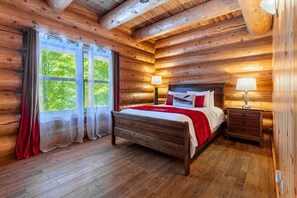 Camera da letto in una casetta di legno con un letto, due comodini e una finestra con tende.