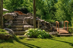 Una scala in pietra conduce a un ponte di legno che sovrasta un piccolo ruscello, immerso nel verde.