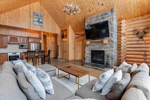 Interno di una baita di legno con camino in pietra, mobili in legno e televisore.