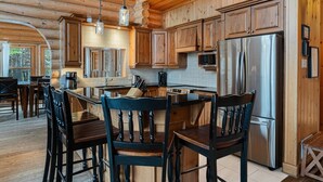 A log cabin interior with a kitchen island, wooden cabinets, and a stainless steel refrigerator. - Fiddler Lake Resort - Elk 96 (Mille-Isles)
