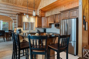 Interno di una baita in legno con un'isola nella cucina, mobili in legno e un frigorifero in acciaio inossidabile.