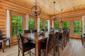 A log cabin interior with a large dining table, multiple chairs, and two chandeliers.