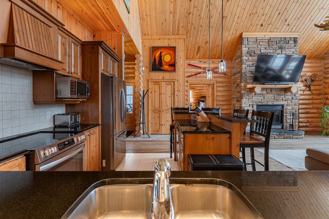 Interior de una cabaña de troncos con cocina, comedor y chimenea de piedra.