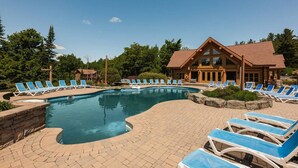 A swimming pool with lounge chairs, a wooden lodge, and surrounding greenery. - Fiddler Lake Resort - Elk 96 (Mille-Isles)