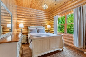 Une chambre située dans un chalet en rondins, avec un lit, des tables de chevet et une grande fenêtre avec des rideaux.