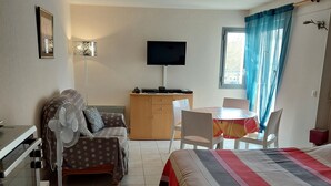 A hotel room with a bed, a desk, a chair, a television, and a window with curtains. - Meublé de Tourisme 3 Étoiles en Résidence Sécurisé (Cap d'Agde)