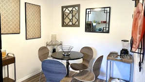 Un coin repas comprenant une table ronde, quatre chaises, un ventilateur de plafond et une petite étagère avec des verres.