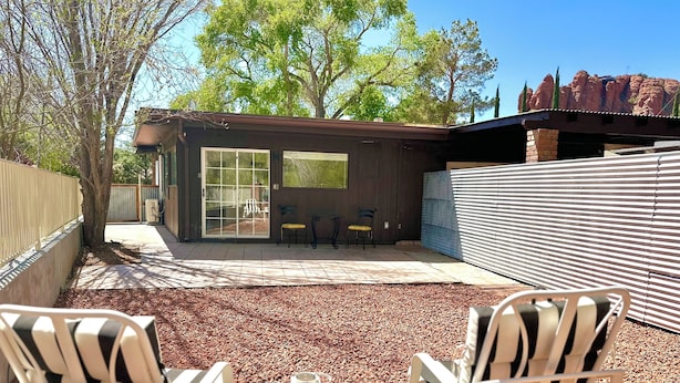 Un espace patio comprenant deux fauteuils Adirondack, une petite table ronde et une porte-fenêtre coulissante donnant sur un espace extérieur aménagé et abrité.