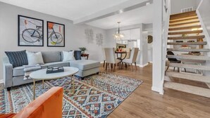 Un salon moderne avec un canapé gris, un tapis à motifs et un escalier menant à l’étage supérieur.