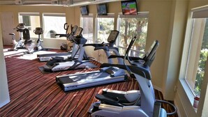 Un gimnasio con varias cintas de correr, bicicletas estáticas y suelo alfombrado.