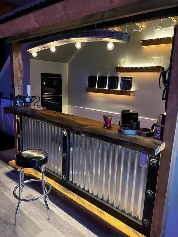 Una zona de bar con mostrador de madera, taburetes y un refrigerador.