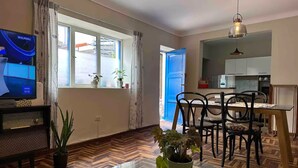 Una sala de estar moderna con televisor, mesa de comedor, sillas y una cocina visible a través de una puerta abierta.