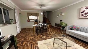 Una sala de estar con piso de parquete, un sofá, una mesita de centro y un comedor con sillas y una mesa.