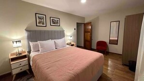 Un dormitorio con una cama grande, mesitas de noche, una silla roja y cuadros enmarcados en la pared.