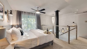 A modern bedroom with a bed, a ceiling fan, a nightstand, and a view of a balcony with a railing. - Modern loft with king suite, resort pool, and historic charm in Swiss Avenue. (Dallas)