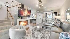 A modern living room with a fireplace, a large TV, and a staircase. - Modern loft with king suite, resort pool, and historic charm in Swiss Avenue. (Dallas)