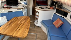 A compact RV interior with a wooden table, blue seating, a kitchenette, a bed, and a TV. - Yacht rental Downtown Providence (Providence)