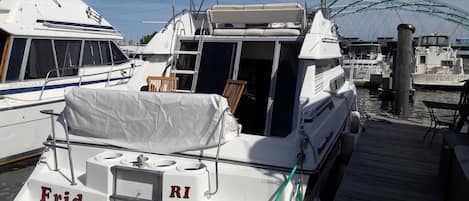 Un barco amarrado en un puerto deportivo con una zona de estar cubierta y el nombre 'Frida Providence' en el costado.