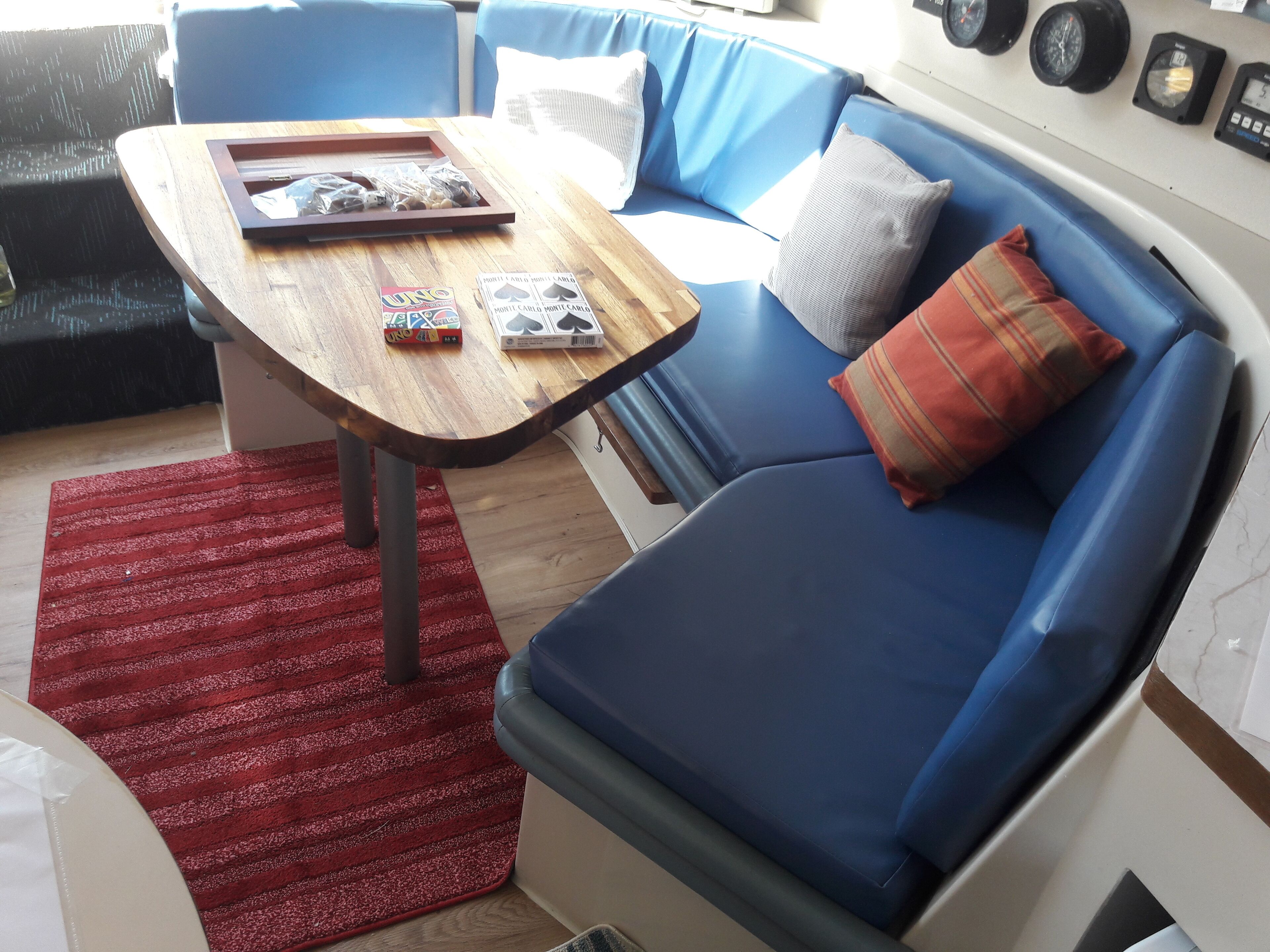 A compact living space with a blue sofa, a wooden table with UNO cards, and a red rug.