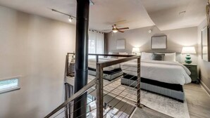 Une chambre avec un grand lit, un ventilateur de plafond, une colonne noire et un escalier doté d’une rampe en métal.