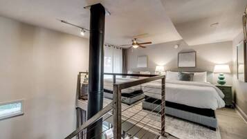 A bedroom with a large bed, a ceiling fan, a black column, and a staircase with a metal railing.